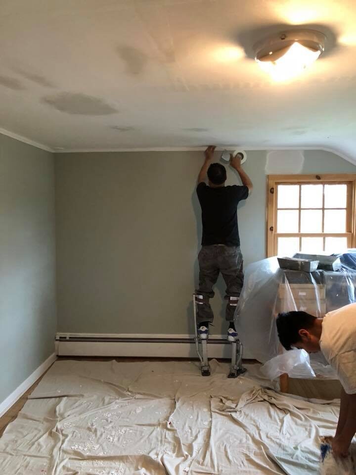 Painter taping a ceiling line with floors and furniture covered by drop cloths