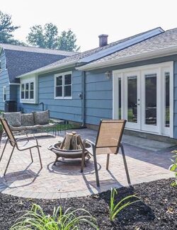 Paver patio with a fire pit and chairs beside a blue sided house