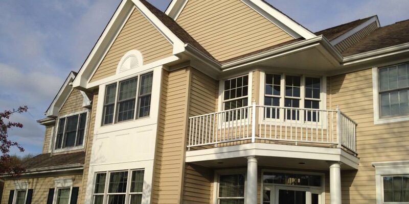 Well-kept colonial with tan siding and white trim after an exterior repaint